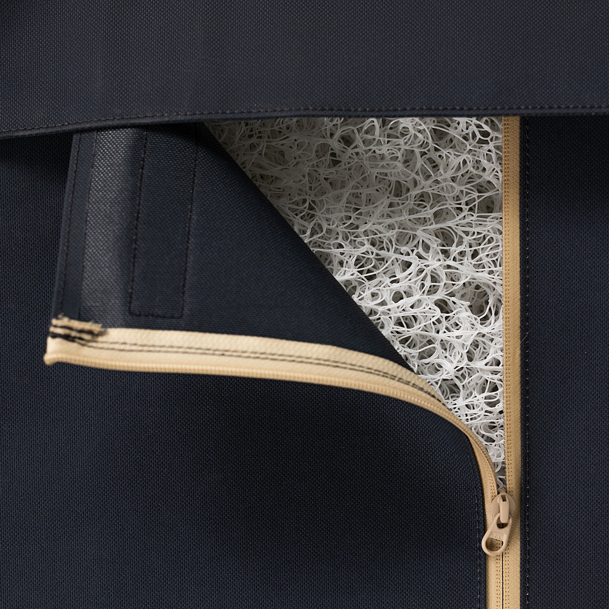 A close-up of a black zippered fabric dog crate cover, partially opened to reveal a white, mesh-like, tangled material inside. The beige zipper opens diagonally across the kennel-themed image.