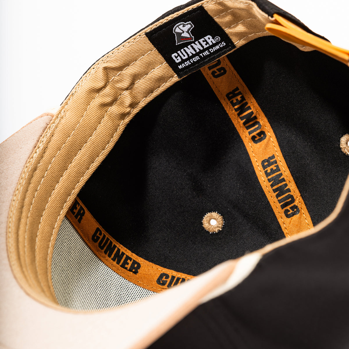 Close-up view of the inside of the GUNNER HUNT SOLIDS Rope Hat, with orange and black GUNNER branding on the seam tape, a black GUNNER MADE FOR THE DAWGS label, and beige and black fabric sections.