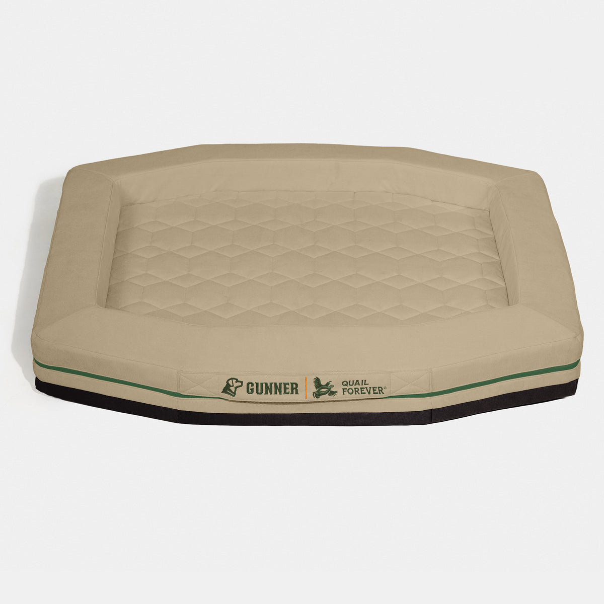 A tan, hexagonal dog bed with a quilted surface—perfect for a working dog to rest comfortably after a long day. The front has Gunner and Quail Forever logos in green, separated by a bird silhouette. Designed to fit seamlessly inside your kennel or dog crate, the bed features a raised edge and a black base.
