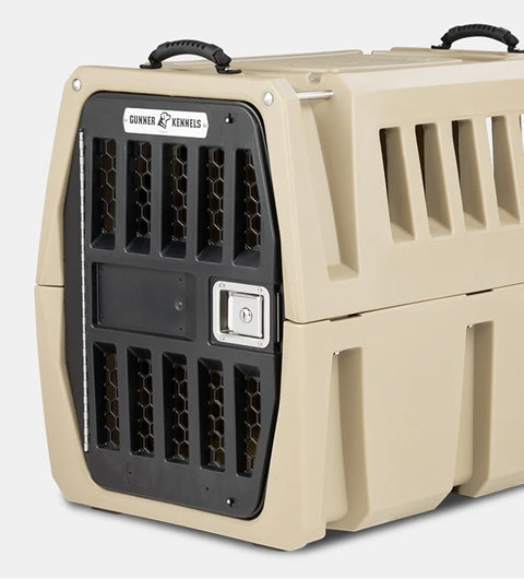 A beige plastic dog kennel with a sturdy black metal door, ventilation slats on the sides, a secure lock, and carrying handles on top. The crate has a Gunner Kennels label on the front—perfect outdoor gear for safe pet travel.