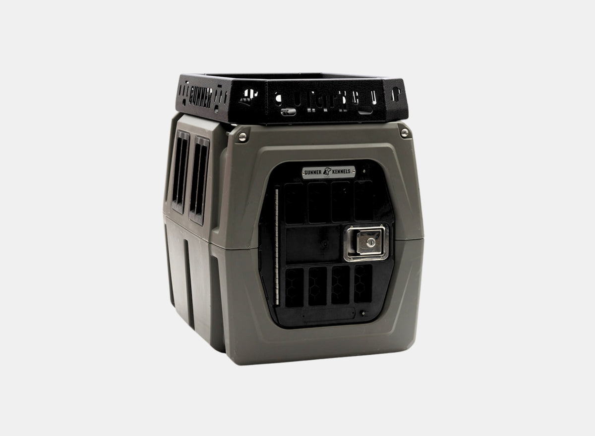 A durable, gray and black plastic Kennel Rack BLACK by GUNNER, featuring ventilation holes and a metal latch on the front door, designed to fit seamlessly into your truck bed or integrate with a kennel storage system, is shown on a plain white background.