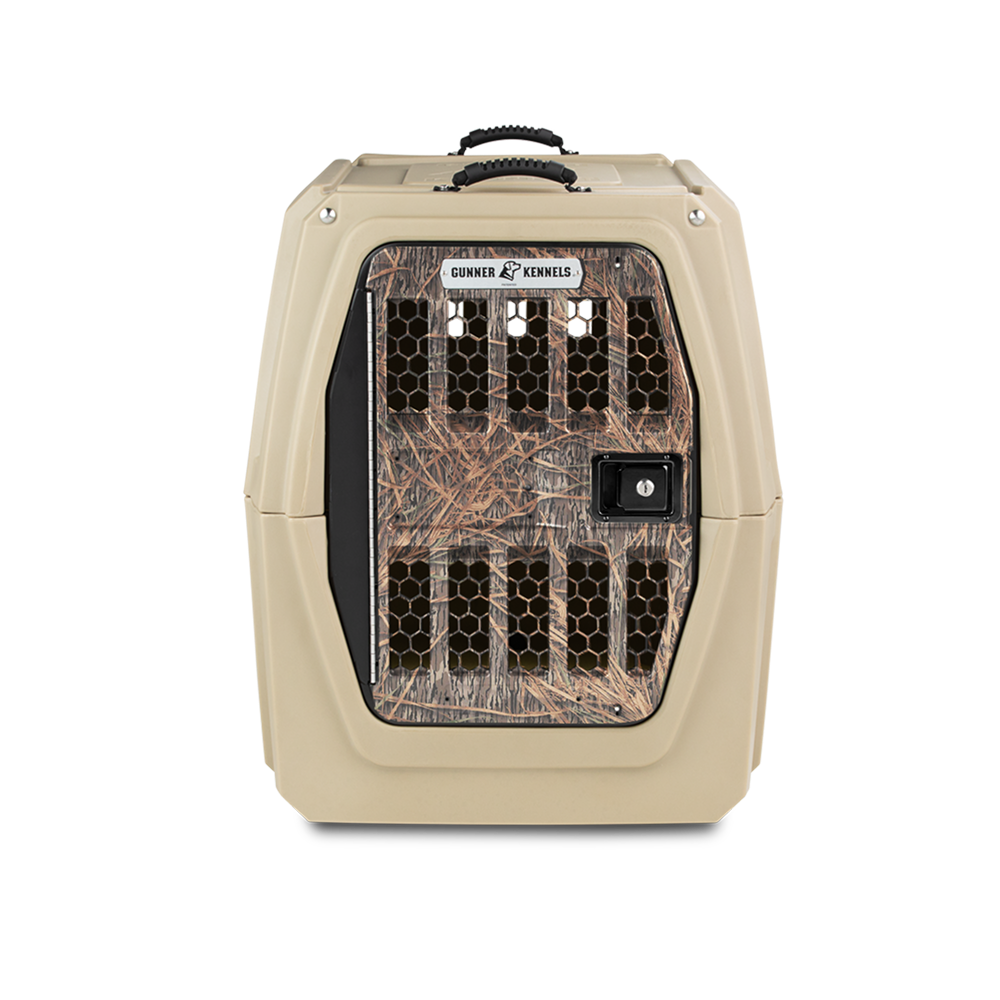 The GUNNER G1™ Kennel in Tan/Shadow Grass features a Mossy Oak-patterned metal door with ventilation holes, a secure latch, and brand logo on the front.