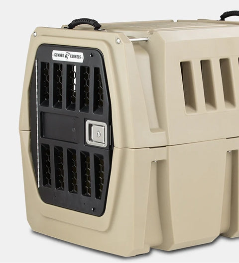 A heavy-duty beige plastic dog kennel with a black metal door, ventilation slats on the sides, and sturdy handles on top, designed for safely transporting working dogs or other animals.