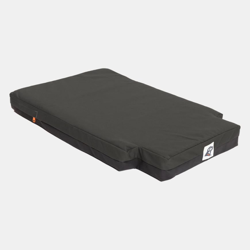 A rectangular, dark gray dog bed with a removable cover and a small logo tag on one corner, designed to complement outdoor gear or fit perfectly inside a kennel, placed on a plain white background.