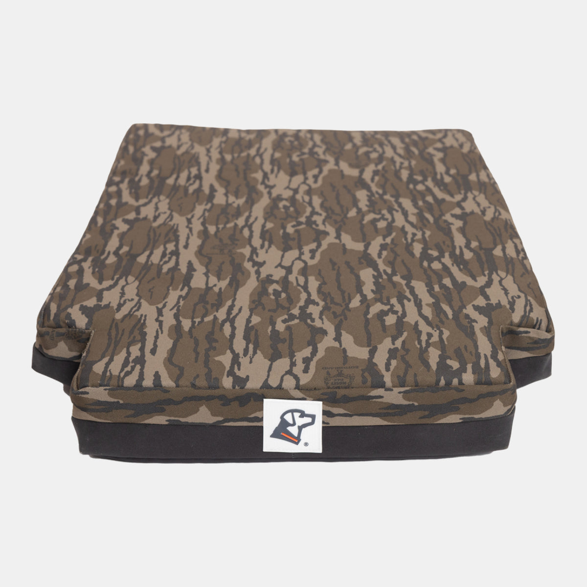 A rectangular cushion with a brown and black camouflage pattern, designed for use in a dog crate or kennel, featuring a small white label with a logo on the front, set against a plain white background.