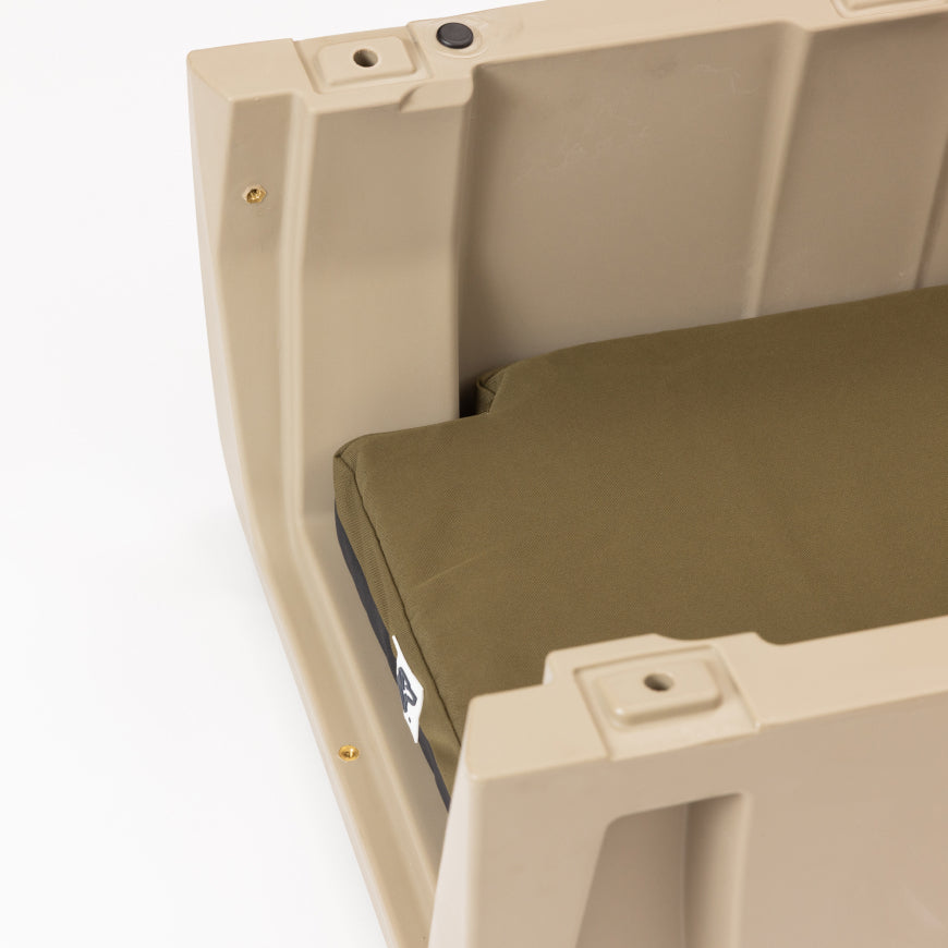 A khaki-colored plastic dog crate with an olive green rectangular cushion inside, photographed from above and slightly to the side against a white background—an essential piece of outdoor gear for pet owners.
