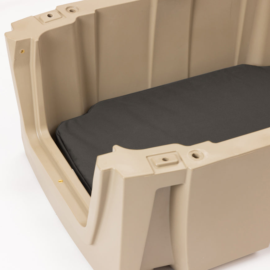 A close-up of a beige plastic container with a black rectangular cushion inside, placed on a white surface. Designed as durable outdoor gear, the container has visible screws and molded edges, making it ideal for use as a kennel for your hunting dog.