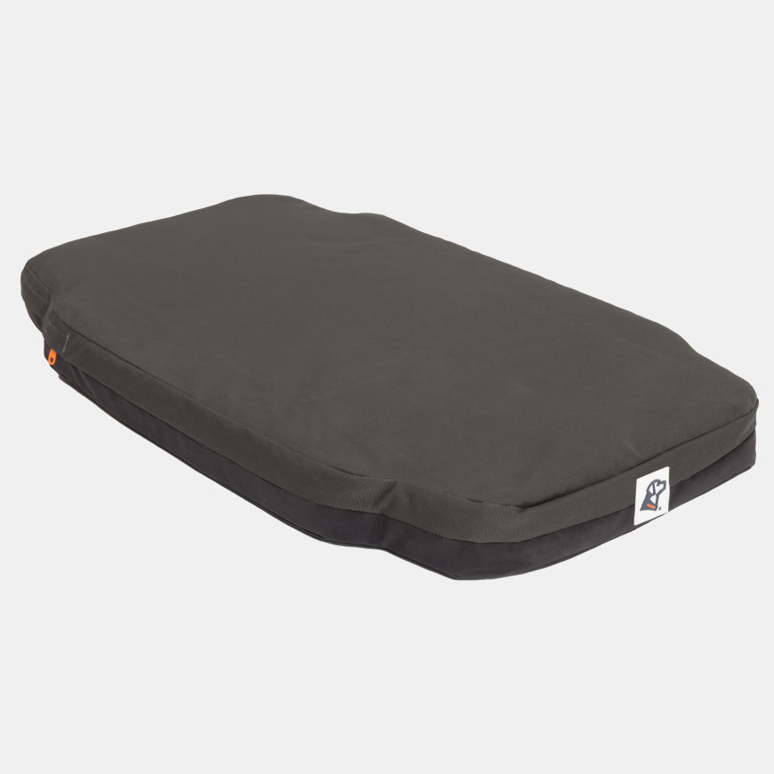 Rectangular, dark gray pet bed with a slightly raised edge, black base, and a small logo patch on the front right corner—designed to fit comfortably inside a standard dog crate—displayed on a plain white background.