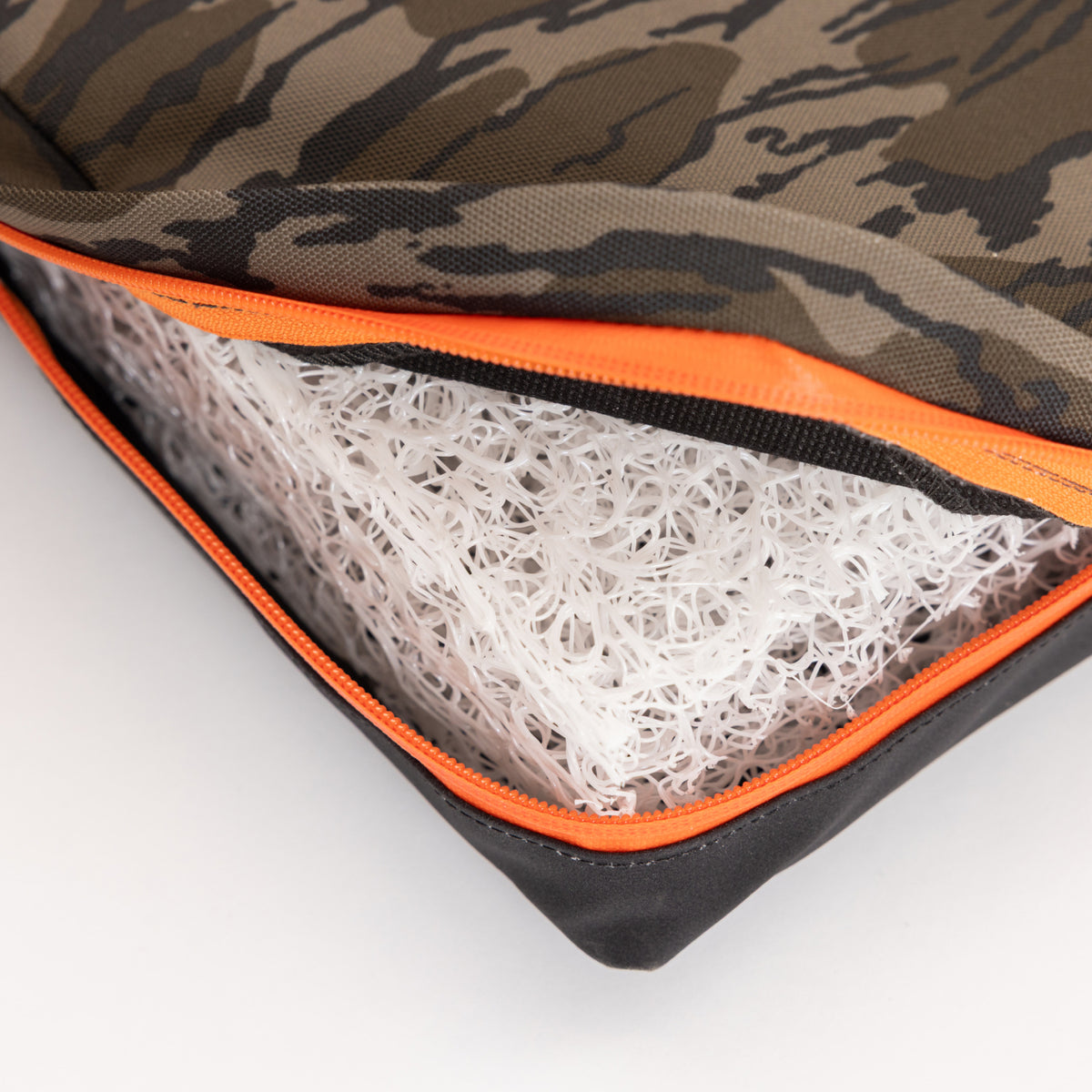 A close-up of a zippered bag with a camouflage pattern, partially open to reveal a white, mesh-like plastic material inside. Designed for outdoor gear enthusiasts and working dog handlers alike, the zipper is orange and bag edges are black.