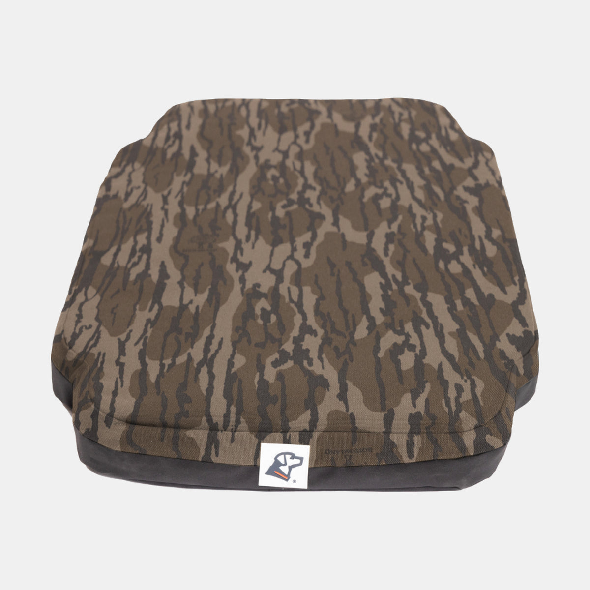 A rectangular, camouflage-patterned pet bed, perfect for a hunting dog or as a cozy addition to any dog kennel, with a small white tag featuring a blue and red logo on the front edge, set against a plain white background.