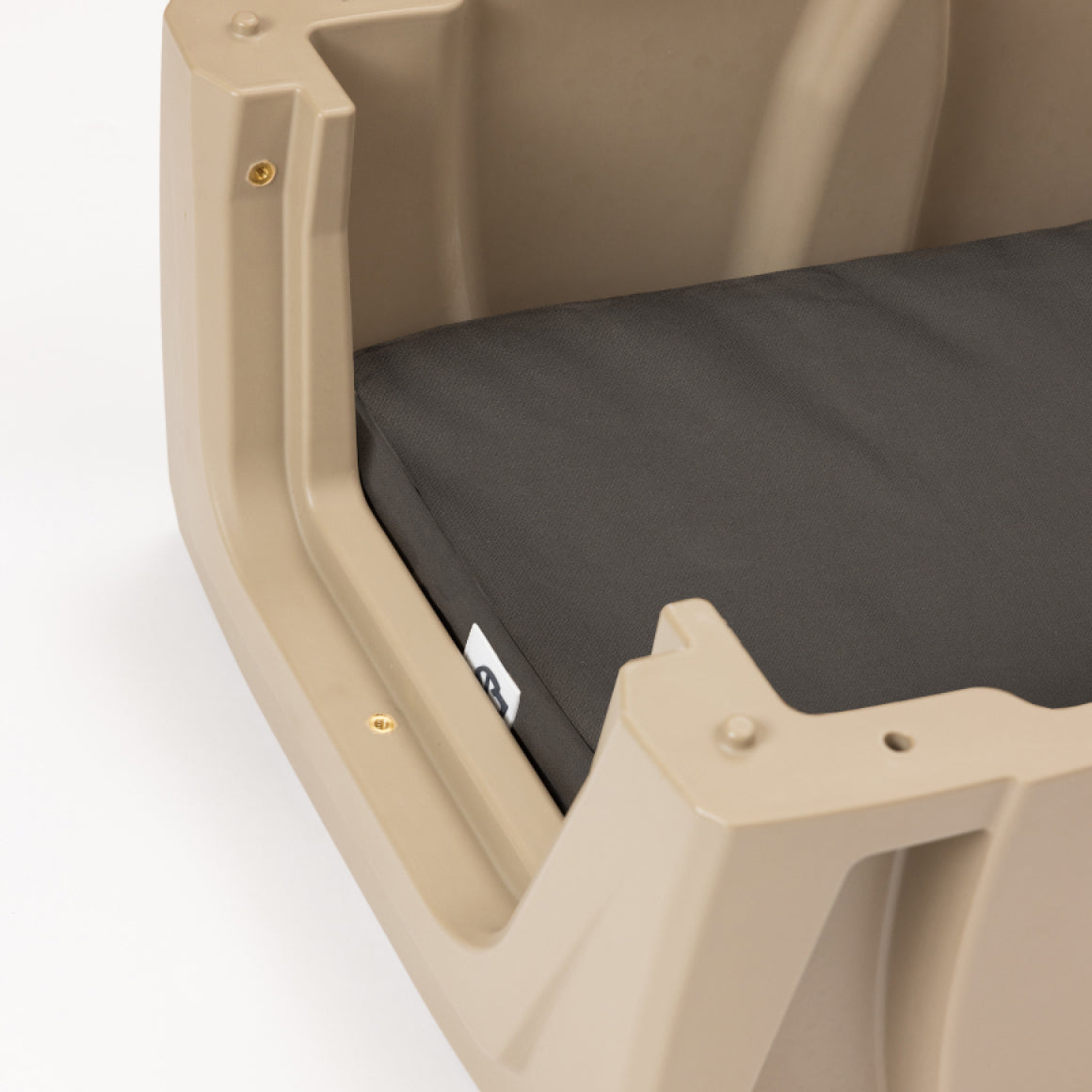 Close-up of a tan plastic pet bed with a dark gray cushion inside. Designed with the durability of outdoor gear in mind, the bed has angular edges and visible screws for added sturdiness—perfect for a hunting dog or working dog needing reliable rest. A small fabric tag is attached to the cushion.