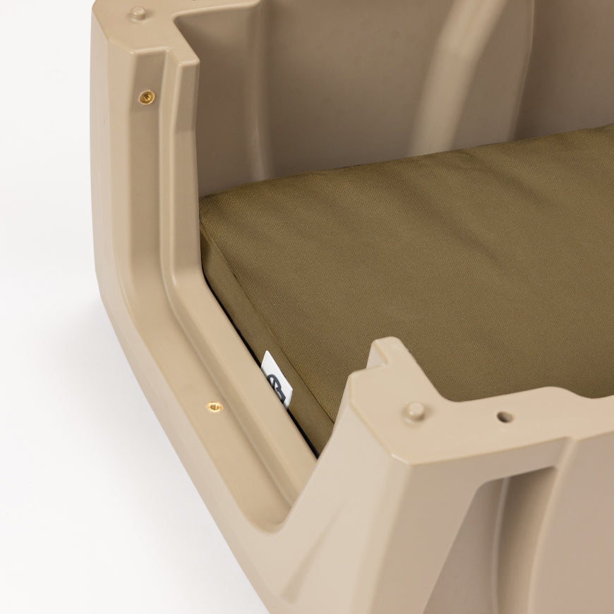 Close-up of a tan plastic pet bed with a green cushion inside, partially revealing a small white tag on the cushion. Perfect for use in a dog crate or kennel, this cozy bed offers comfort whether at home or while resting after a long day for your hunting dog. The background is plain white.