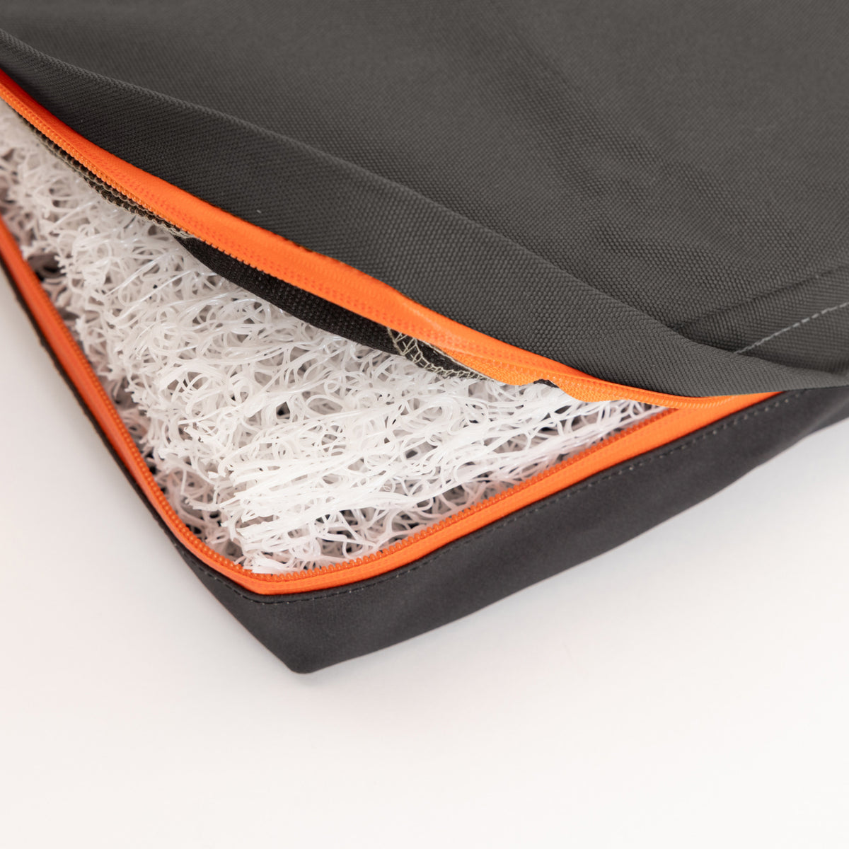 A close-up of a black and orange zippered cover, reminiscent of rugged outdoor gear, partially open to reveal a white, mesh-like cushion inside.