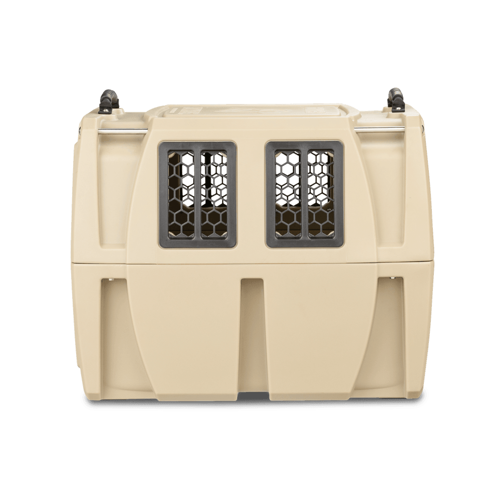 The GUNNER G1™ KENNEL - MOSSY OAK BOTTOMLAND TAN is a tan plastic dog crate with two front mesh windows and black top handles, designed for safe and comfortable travel, shown against a white background.