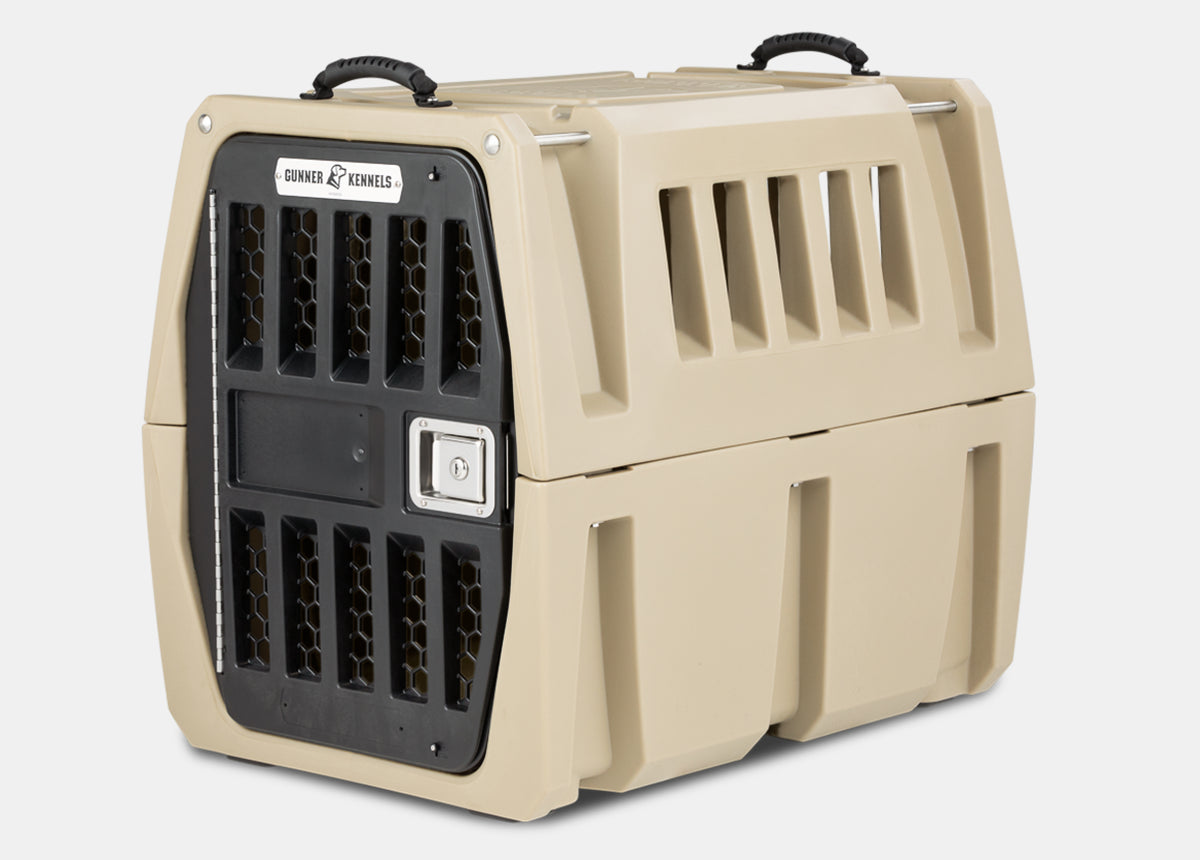 A tan and black heavy-duty plastic dog crate with ventilation holes, a secure metal door, side handles, and the Gunner Kennels logo on the front—perfect outdoor gear for any working dog.