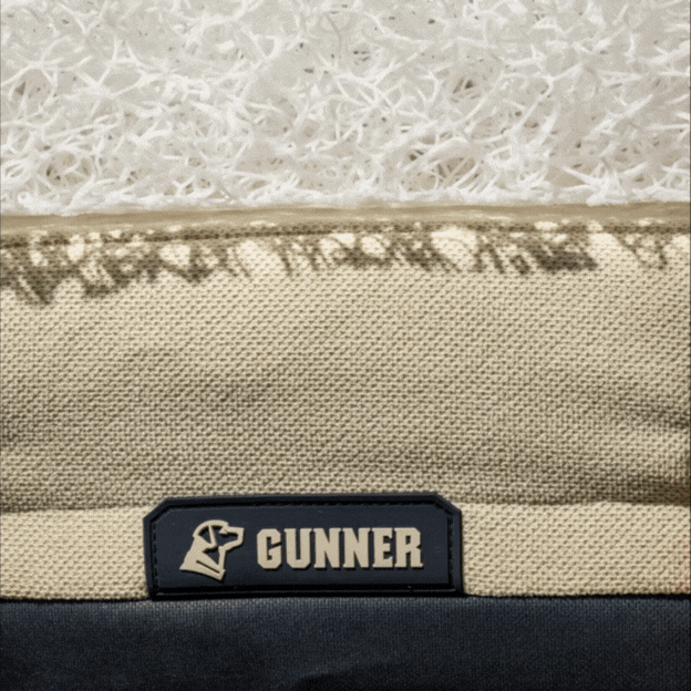 Close-up of a beige and cream textured pet bed, perfect for dog kennel or crate use, with a label featuring a dog’s head silhouette and the word “GUNNER” stitched on a navy patch.