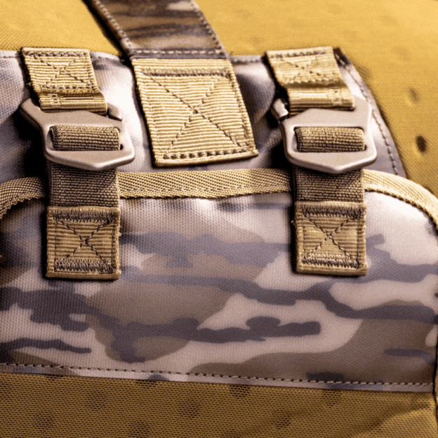 Close-up of a camouflage-patterned backpack with tan straps and metal buckles, showcasing detailed stitching and fabric texture—perfect for carrying your outdoor gear on dog kennel trips.