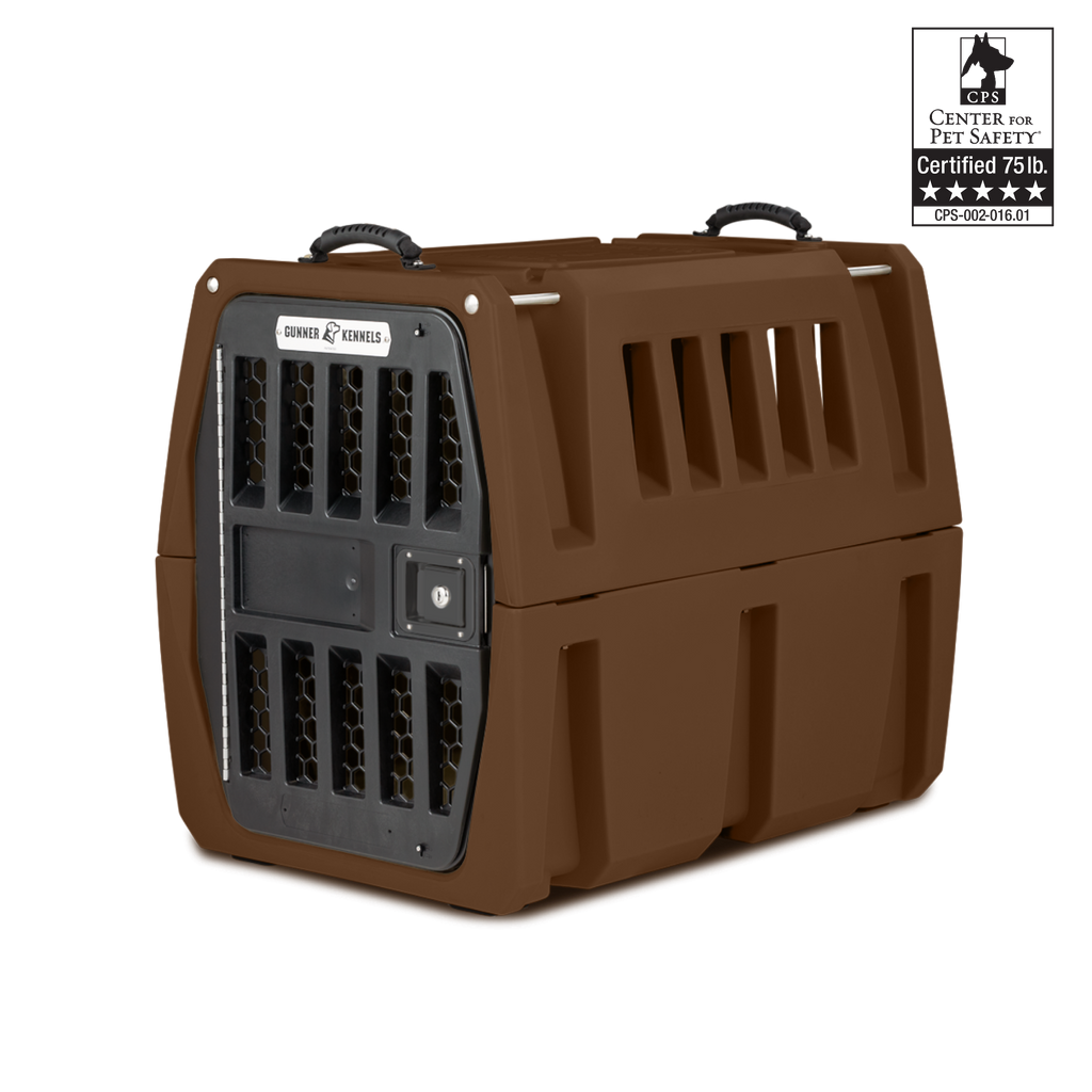 A brown hard-sided dog kennel with a black metal door and ventilation slots, featuring a certification label for 75 lb. pet safety in the top right corner. The kennel includes handles on top for carrying your working dog securely.