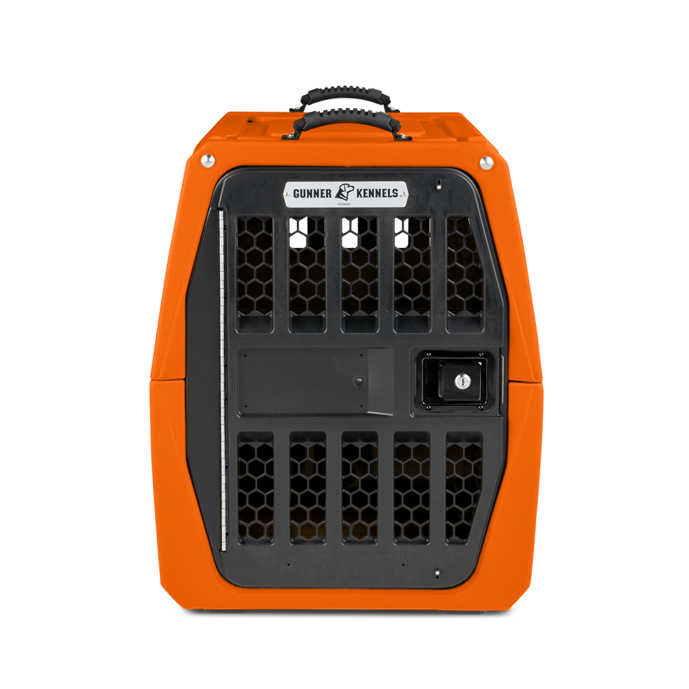 An orange, hard-shell dog kennel with a black metal door featuring hexagonal ventilation holes and a secure latch. The top handle is visible, and a Gunner Kennels label is on the front—ideal for keeping your working dog safe.