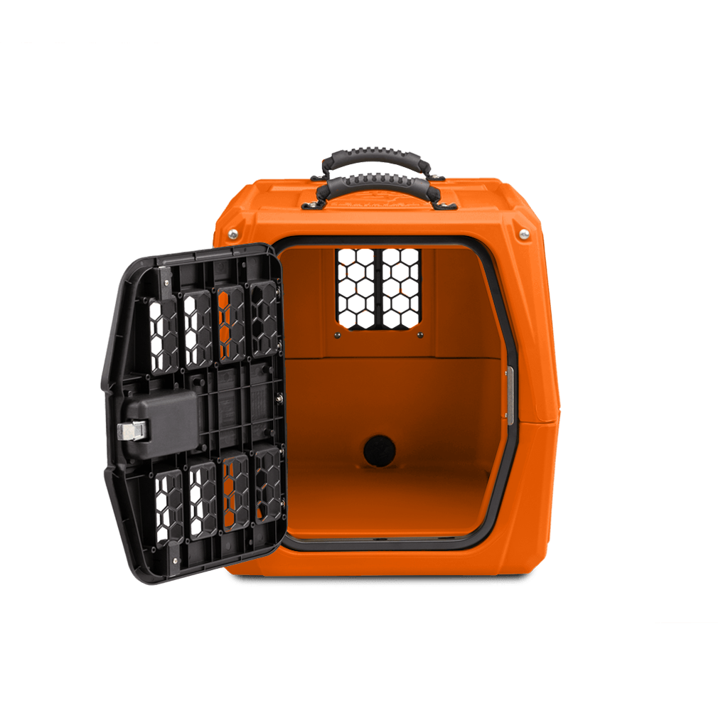 An orange hard-shell dog kennel with a black, grated door open to the left, showing the empty interior and ventilation holes. The pet carrier has a handle on top and is placed against a plain white background.
