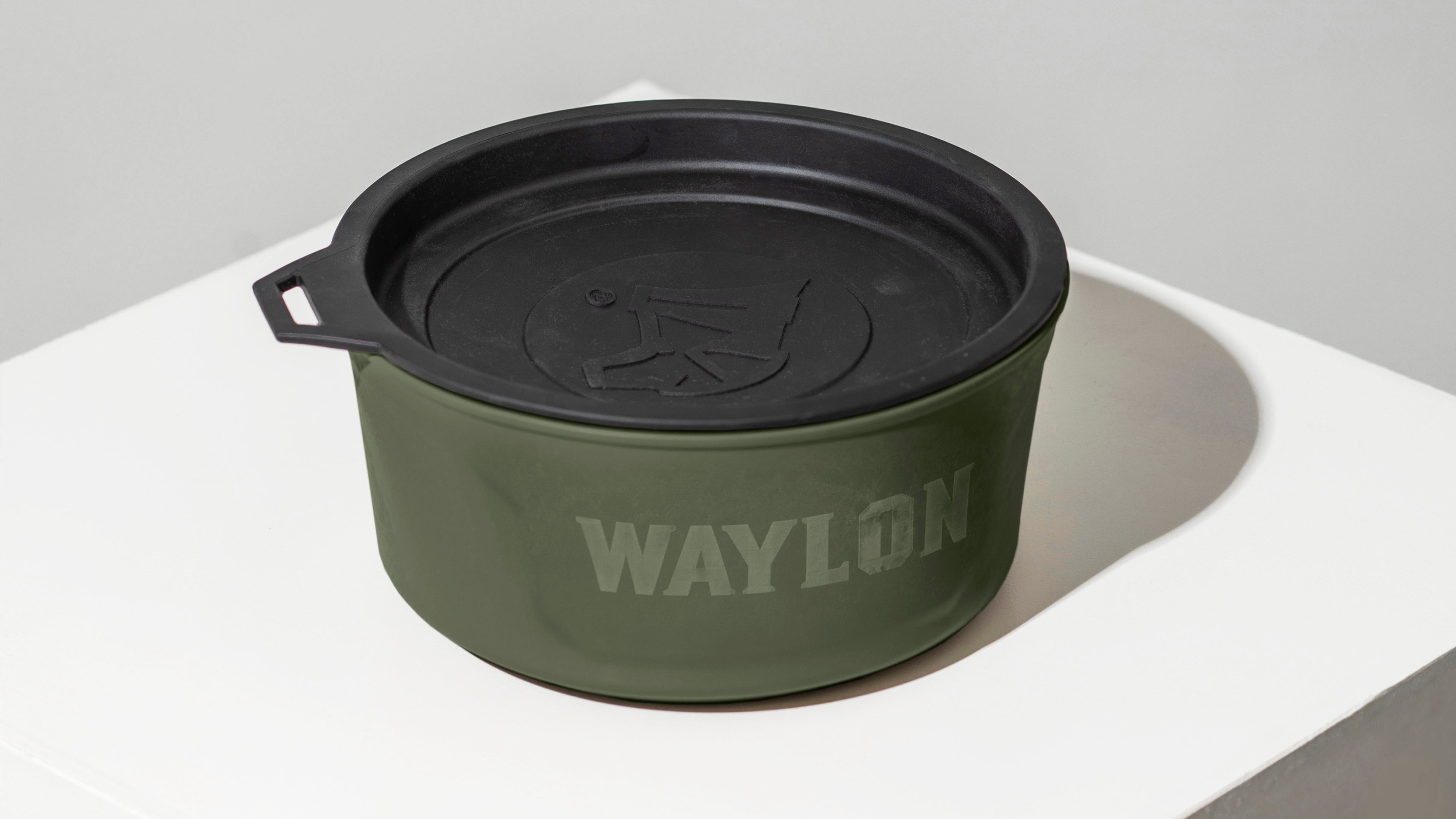 A green container with a black lid and small handle sits on a white surface. The word WAYLON is printed on the side, making it perfect for storing treats or gear for your hunting dog or in the kennel. The lid features a raised logo.