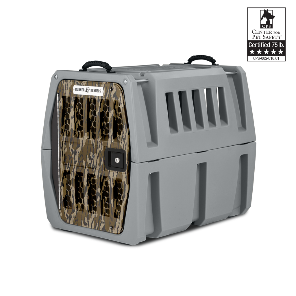 A sturdy gray dog kennel with a camouflage-patterned door, black handles on top, and ventilation slats is shown on a white background. Ideal outdoor gear for your working dog. A “Certified 75 lb.” Center for Pet Safety logo appears in the upper right corner.