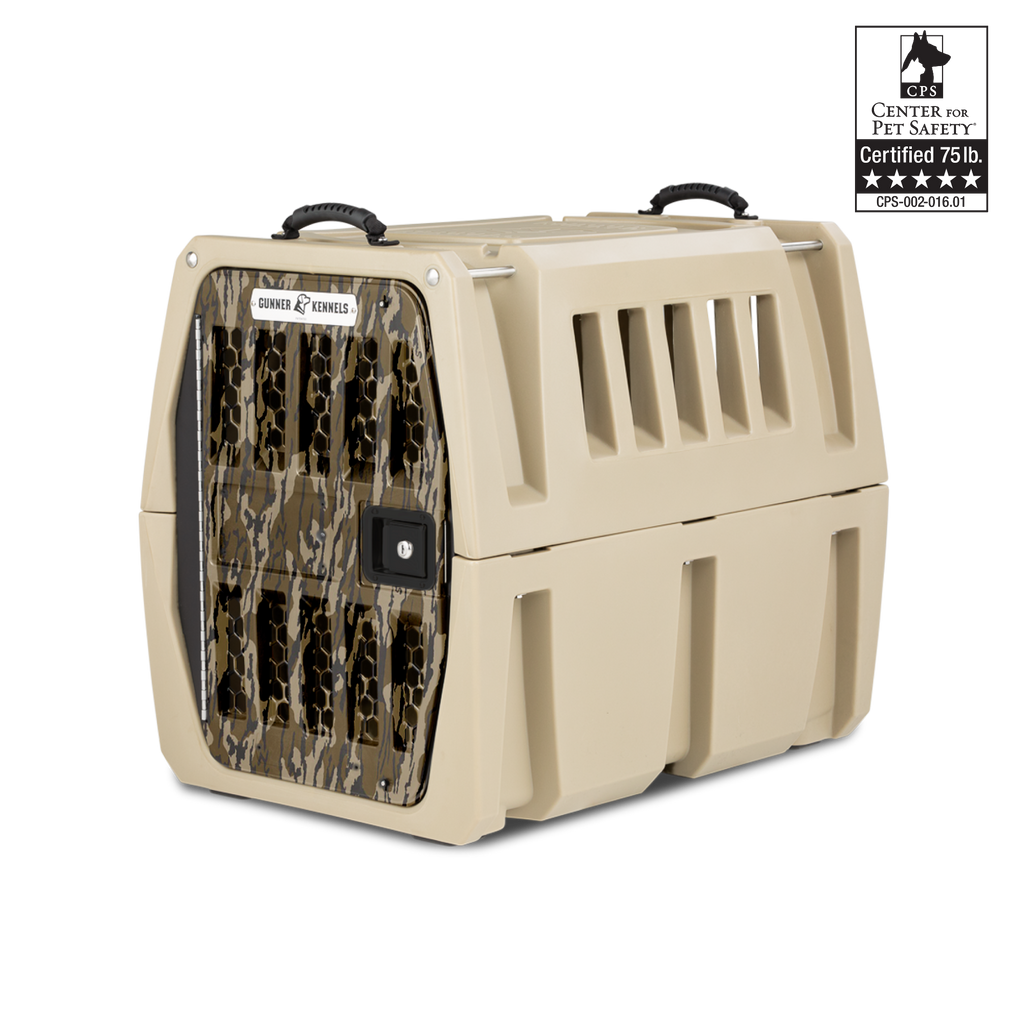 A tan, hard-sided dog crate with a camouflage-patterned door, ventilation slats, black handles, and a label showing it is Center for Pet Safety certified for hunting dogs up to 75 lbs.