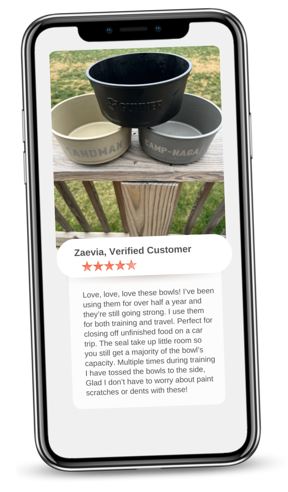 A phone displays a photo of three dog bowls labeled SANDMAN, CAMP-NAGO, and PAWDURE, stacked on a wooden surface. Below, a 5-star customer review praises the bowls durability and reliability for travel or use in a dog kennel.