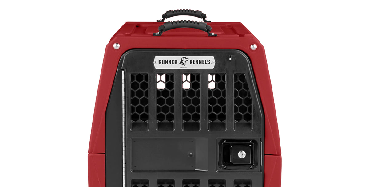 A red and black kennel with a metal label reading Gunner Kennels above a ventilated door featuring a secure latch and handle on top, ideal for transporting your hunting dog or working dog safely.