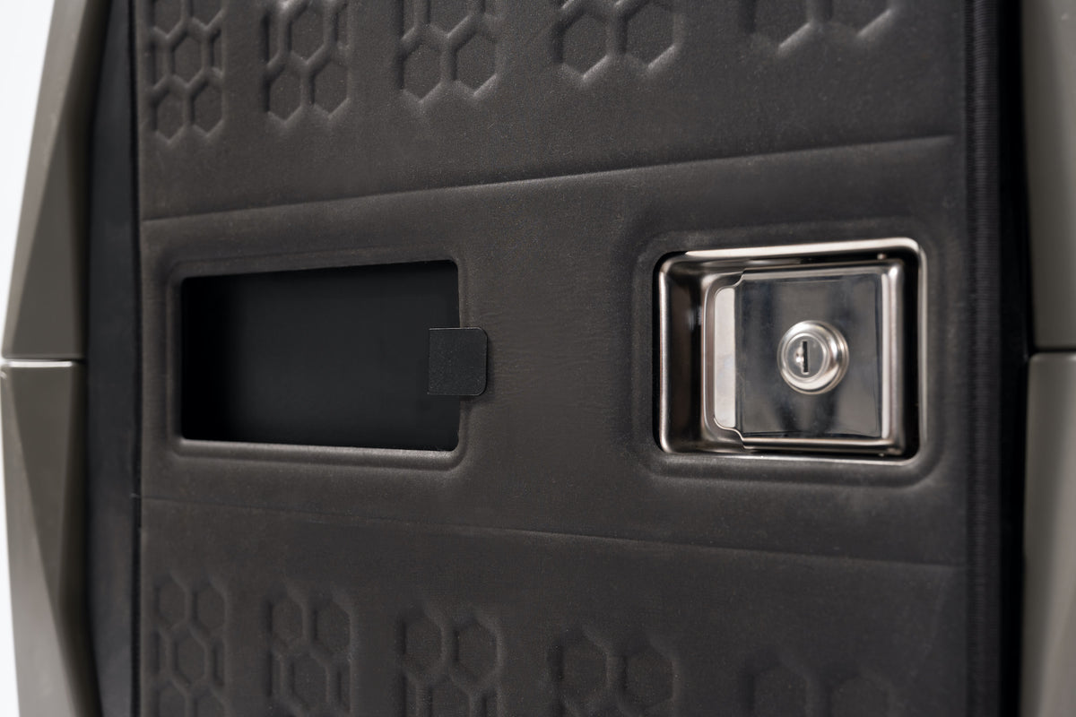 Close-up of the GUNNER COLD WEATHER DOOR COVERs textured black panel, highlighting a rectangular slot on the left and a metallic, lockable latch on the right; its surface has a geometric pattern, similar to durable thermoformed foam.
