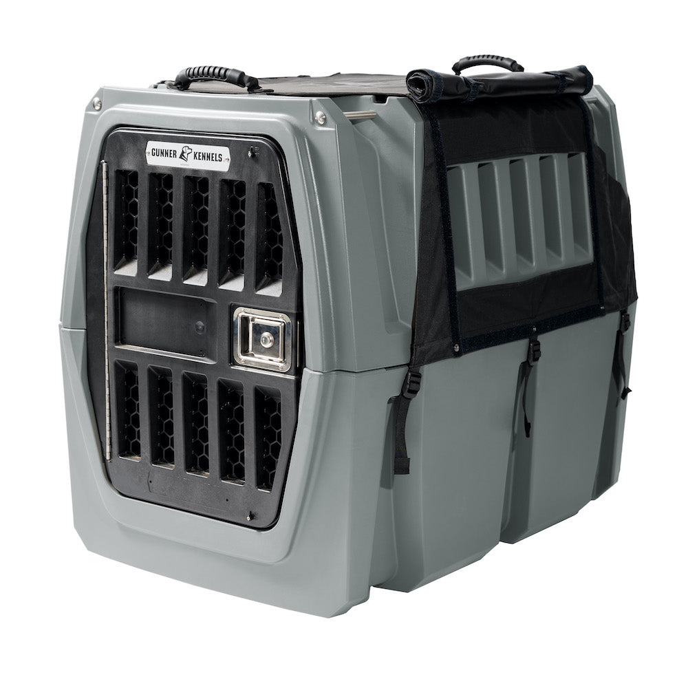 A sturdy gray GUNNER dog crate with ventilation holes, a metal locking door, black top handles, and reinforced sides—compatible with the ALL-WEATHER KIT 2.0 for added UV protection and a waterproof kennel cover for secure pet transport.
