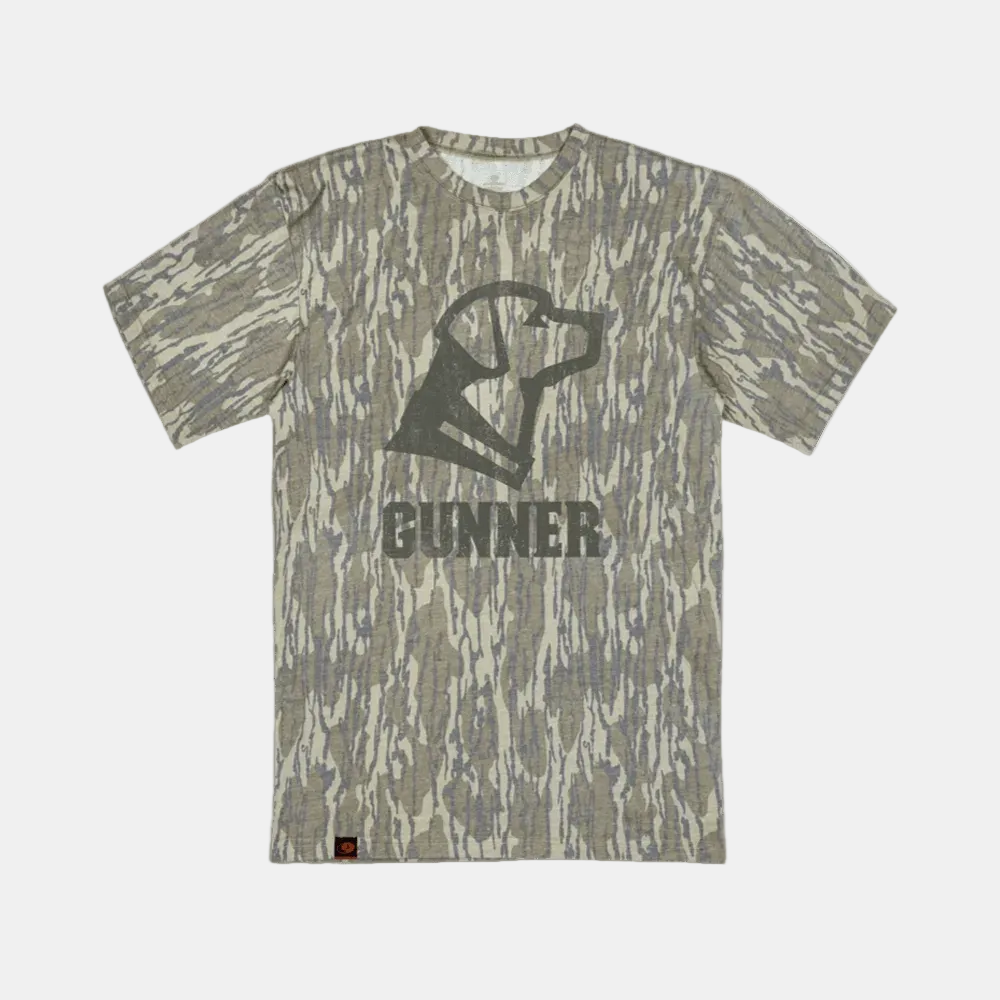 The GUNNER BOTTOMLAND TEE is a triblend crew neck with short sleeves, featuring a Mossy Oak Bottomland camo print and a stylized dog head graphic above the word GUNNER on the front.