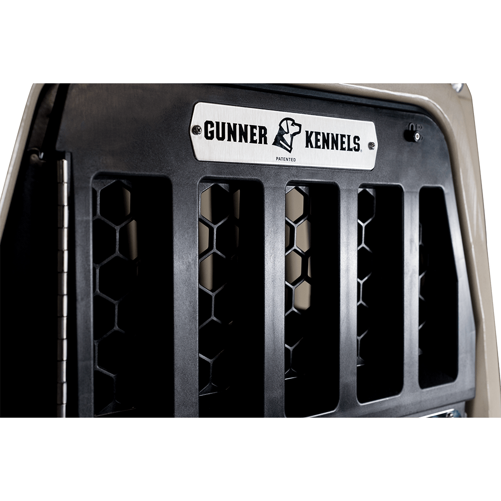 Close-up of the GUNNER G1™ KENNEL DOOR showing black hexagonal vents, a custom welded aluminum frame, and a metal nameplate with the GUNNER logo on a beige background.