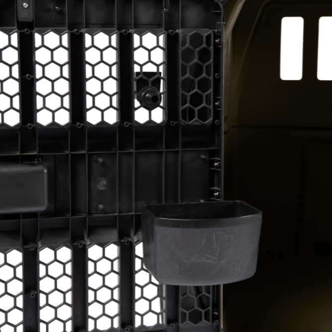 Close-up view of the G1 Kennel interior with a black plastic door featuring hexagonal vents. The attached KENNEL BOWL helps keep your dog hydrated as light filters through the crate’s openings.
