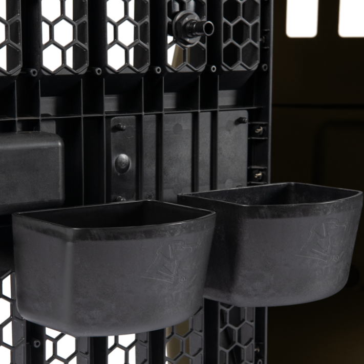 Close-up of two KENNEL BOWLs attached to a grid panel, likely inside a G1™ Kennel. Positioned where light filters through vented openings, these bowls are designed for easy dog hydration on the go.